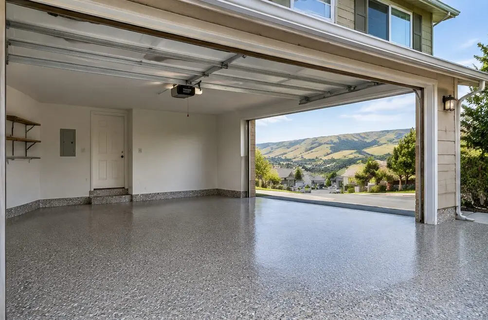 Illustration: a clean two-car Mission-Garin garage with a full-broadcast gray-and-tan flake epoxy floor and a coated curb at the garage door